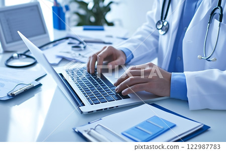 High-definition scene of a doctor's hands, operating a laptop computer and handling medical documents 122987783
