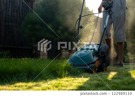 Border of the mown grass on the lawn, sunny day at sunset, low angle view. Green grass in the backyard, electric lawn mower. 122989110