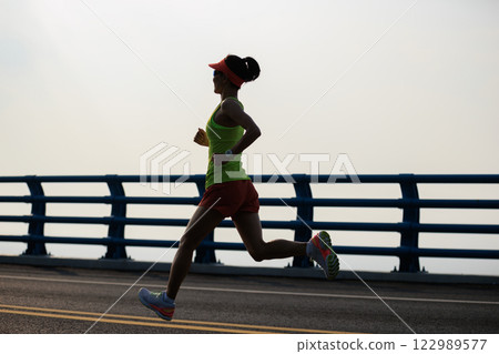 Healthy lifestyle woman runner running on seaside bridge 122989577