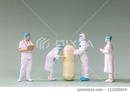 Tiny figurines of doctors and scientists examining an oversized medical capsule Tiny figurines of doctors and scientists examining an oversized medical capsule 122989844