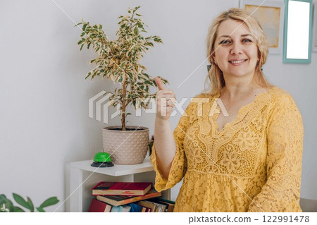 cheerful woman in yellow giving thumbs up in a bright office, concept of success coaching, motivational speaking, personal branding 122991478