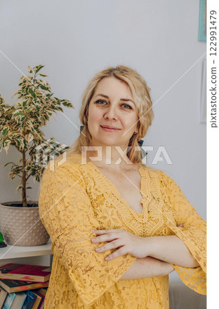 confident woman standing in a room with a serene smile in yellow, concept of personal coaching, wellness retreats, professional development 122991479