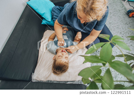 smiling boy lying on a soft blanket during a therapy session with a female specialist in a cozy room, concept of relaxation, childhood therapy, and healthcare smiling boy lying on a soft blanket during a therapy session with a female specialist in a cozy room, concept of relaxation, childhood therapy, and healthcare 122991511