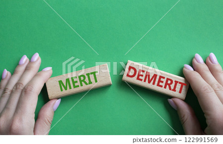 Merit or Demerit symbol. Concept word Merit or Demerit on wooden blocks. Businessman hand. Beautiful green background. Business and Merit or Demerit concept. Copy space Merit or Demerit symbol. Concept word Merit or Demerit on wooden blocks. Businessman hand. Beautiful green background. Business and Merit or Demerit concept. Copy space 122991569