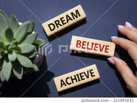 Dream Believe Achieve symbol. Wooden blocks with words Dream Believe Achieve. Businessman hand. Beautiful deep blue background with succulent plant. Business and Dream Believe Achieve concept. Copy 122991632