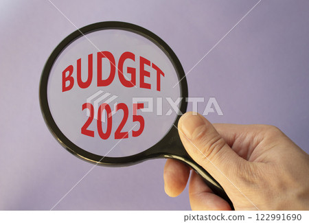 Budget 2025 symbol. Magnifying Glass with words Budget 2024. Beautiful purple background. Businessman hand. Business and Budget 2025 concept. Copy space. Budget 2025 symbol. Magnifying Glass with words Budget 2024. Beautiful purple background. Businessman hand. Business and Budget 2025 concept. Copy space. 122991690