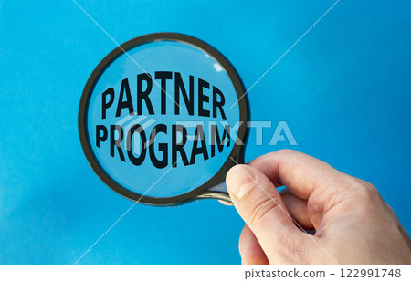 Partner Program symbol. Concept words Partner Program on magnifying glass. Businessman hand. Beautiful blue background. Business and Partner Program concept. Copy space. 122991748