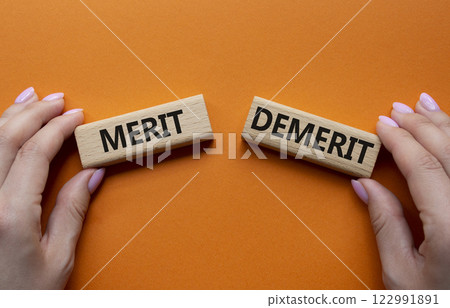 Merit or Demerit symbol. Concept word Merit or Demerit on wooden blocks. Businessman hand. Beautiful orange background. Business and Merit or Demerit concept. Copy space 122991891