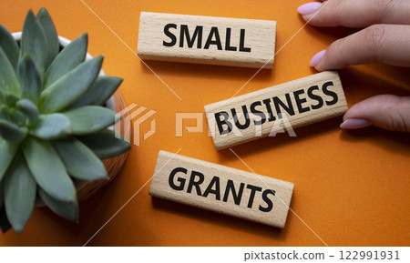 Small Business Grants symbol. Wooden blocks with words Small Business Grants. Beautiful orange background with succulent plant. Businessman hand. Business and Contact us now concept. Copy space. 122991931