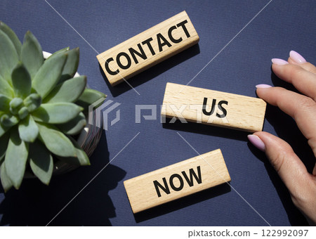 Contact us now symbol. Wooden blocks with words Contact us now. Beautiful deep blue background with succulent plant. Businessman hand. Business and Contact us now concept. Copy space. 122992097