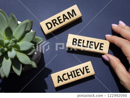 Dream Believe Achieve symbol. Wooden blocks with words Dream Believe Achieve. Businessman hand. Beautiful deep blue background with succulent plant. Business and Dream Believe Achieve concept. Copy 122992098
