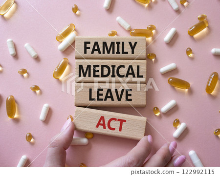 Family Medical Leave Act symbol. Concept word Family Medical Leave Act on wooden blocks. Businessman hand. Beautiful pink background with pills. Medicine concept. Copy space 122992115