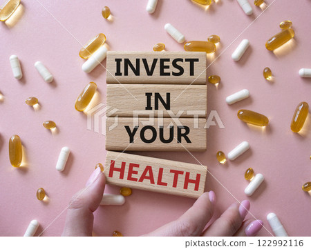 Invest in your Health symbol. Concept word Invest in your Health on wooden blocks. Businessman hand. Beautiful pink background with pills. Medicine concept. Copy space 122992116