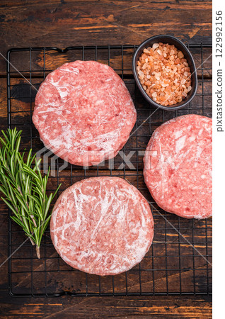 Frozen Meat patties ready for grilling, forcemeat of pork and beef for burgers. wooden background. top view Frozen Meat patties ready for grilling, forcemeat of pork and beef for burgers. wooden background. top view 122992156
