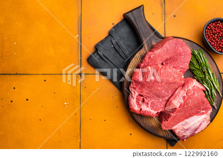 Raw beef fillet tender steaks on a decorative wooden board, fresh meat ready for grill. orange background. top view Raw beef fillet tender steaks on a decorative wooden board, fresh meat ready for grill. orange background. top view 122992160