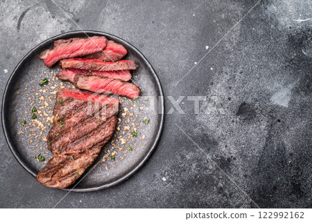 Grilled New York Striploin steak, perfectly seared with beautiful grill marks, showcasing its juicy tenderness and rich flavor. black background. top view 122992162