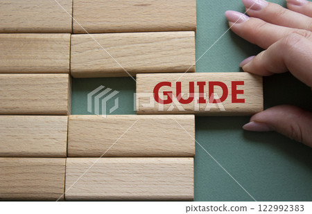 Guide symbol. Concept word Guide on wooden blocks. Beautiful grey green background. Businessman hand. Business and Guide concept. Copy space. 122992383