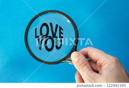 Love you symbol. Magnifying Glass with Concept word Love you. Beautiful blue background. Businessman hand. Love concept. Copy space 122992395