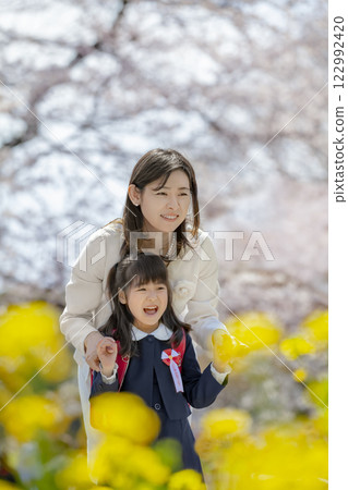 一位母親和她剛出生的女兒在盛開著櫻花和油菜花的公園裡玩耍 122992420