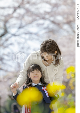 一位母親和她剛出生的女兒在盛開著櫻花和油菜花的公園裡玩耍 122992424