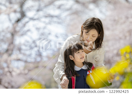 一位母親和她剛出生的女兒在盛開著櫻花和油菜花的公園裡玩耍 122992425