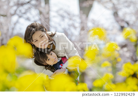 一位母親和她剛出生的女兒在盛開著櫻花和油菜花的公園裡玩耍 122992429