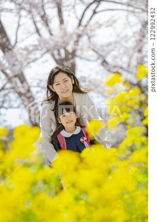 一位母親和她剛出生的女兒在盛開著櫻花和油菜花的公園裡玩耍 122992432