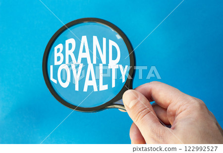 Brand Loyalty symbol. Concept word Brand Loyalty on magnifying glass. Beautiful blue background. Businessman hand. Business and Brand Loyalty concept. Copy space. 122992527