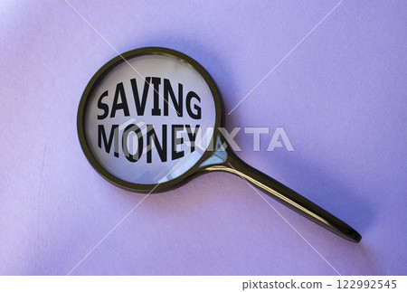 Saving Money symbol. Concept words Saving Money on magnifying glass. Beautiful purple background. Business and Saving Money concept. Copy space. Saving Money symbol. Concept words Saving Money on magnifying glass. Beautiful purple background. Business and Saving Money concept. Copy space. 122992545