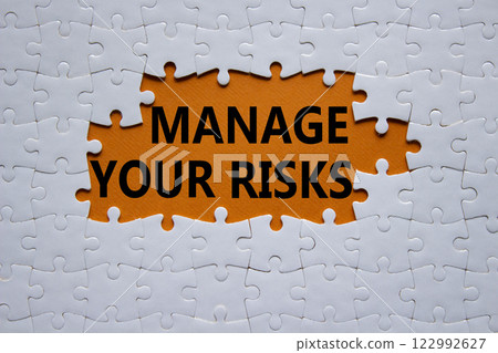 Risks symbol. Concept words Manage your Risks on white puzzle. Beautiful orange background Business and Manage your Risks concept. Copy space. Risks symbol. Concept words Manage your Risks on white puzzle. Beautiful orange background Business and Manage your Risks concept. Copy space. 122992627