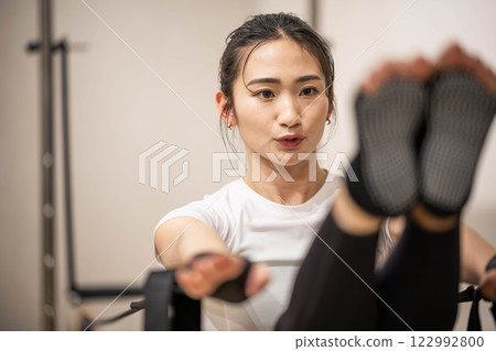 Young woman doing machine pilates in indoor gym Young woman doing machine pilates in indoor gym 122992800