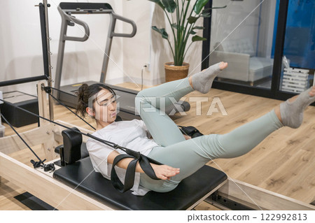 Young woman doing machine pilates in indoor gym Young woman doing machine pilates in indoor gym 122992813