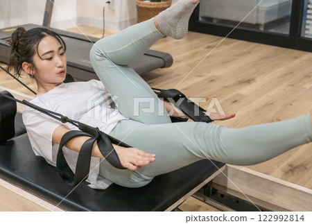 Young woman doing machine pilates in indoor gym Young woman doing machine pilates in indoor gym 122992814