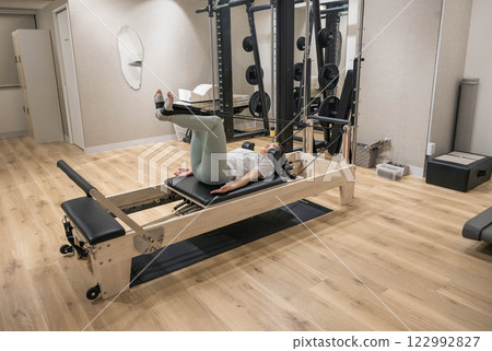 Young woman doing machine pilates in indoor gym Young woman doing machine pilates in indoor gym 122992827
