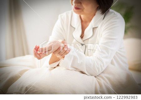 早上，穿著白色睡衣的中年婦女在臥室裡手腕疼痛 122992983
