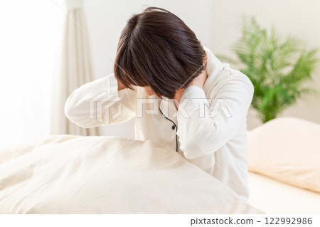 一名身穿白色睡衣的中年婦女早上在臥室裡感到頸部和肩膀僵硬 122992986