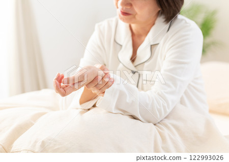 早上，穿著白色睡衣的中年婦女在臥室裡手腕疼痛 122993026