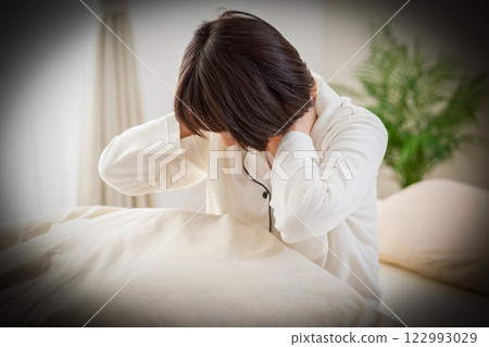一名身穿白色睡衣的中年婦女早上在臥室裡感到頸部和肩膀僵硬 122993029