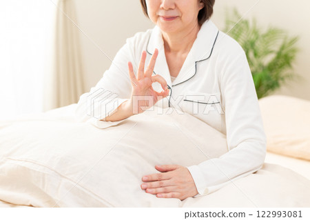 早上，一位身穿白色睡衣的中年婦女在臥室裡微笑著畫著圓圈 122993081