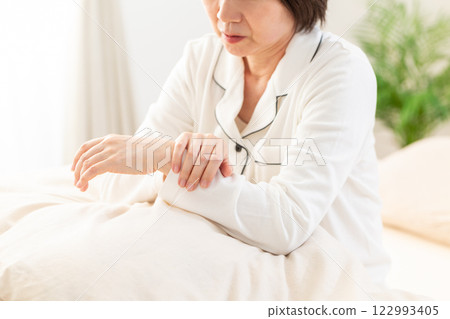 早上，穿著白色睡衣的中年婦女在臥室裡手腕疼痛 122993405