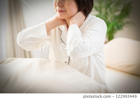 一名身穿白色睡衣的中年婦女早上在臥室裡感到頸部和肩膀僵硬 122993449