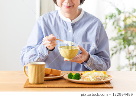 Middle-aged woman eating yogurt for a Western-style breakfast Middle-aged woman eating yogurt for a Western-style breakfast 122994499