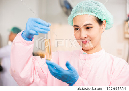 Juice beverage factory woman food engineer emphasizes food and beverage quality and safety testing employing test tubes to sample basil or chia seeds in bottled products in laboratory control. Juice beverage factory woman food engineer emphasizes food and beverage quality and safety testing employing test tubes to sample basil or chia seeds in bottled products in laboratory control. 122995834