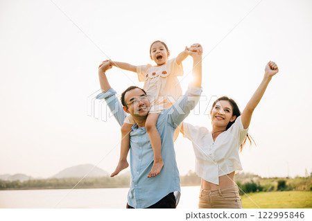 Asian family child girl piggyback riding back on father raising hands like flying outdoor nature park with mother, Happy parent daughter having fun together, Tourist lifestyle family leisure activity 122995846