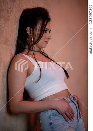 A Stylish Young Woman is Posing Gracefully Against a Wall in Her Casual Yet Trendy Outfit A Stylish Young Woman is Posing Gracefully Against a Wall in Her Casual Yet Trendy Outfit 122997802