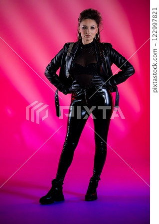 A Stylish Woman Dressed in a Black Leather Outfit Poses Against a Brightly Colorful Background 122997821