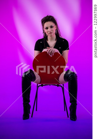 A Stylish Model Is Posing with a Red Chair Positioned Against a Beautiful Pink Background 122997869