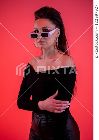 A Fashionable Woman in Stylish Sunglasses Posing Confidently Against a Vibrant Red Background 122997927