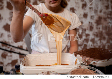 A Young Artist Skillfully Mixing Paint with a Wooden Spoon in Their Modern Studio Space 122998035