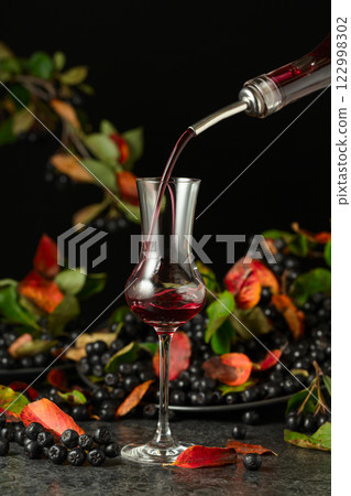 Black chokeberry liqueur and fresh berries on a black table. Black chokeberry liqueur and fresh berries on a black table. 122998302